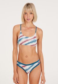 Bikini set s uzorkom tie-dye u plavoj, bijeloj i crvenoj boji. Ima skraćeni top s uskim trakama i odgovarajuće gaće s plavim rubom.