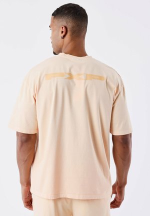 Camiseta de algodón color durazno claro de manga corta, con un gran logo amarillo "PXP" en la parte posterior, de corte holgado y textura suave.