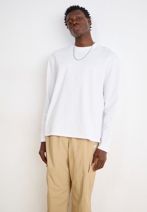 Long-sleeve white cotton shirt with round neckline, paired with tan cargo pants featuring a pocket and subtle branding.