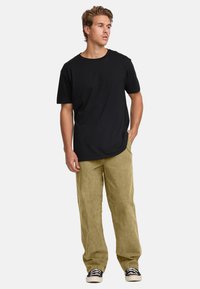 Black cotton T-shirt with short sleeves, paired with light beige corduroy pants. Black and white sneakers with a textured sole.