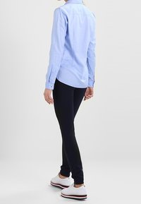 Camicia a maniche lunghe azzurro chiaro con polsini a bottoni, abbinata a pantaloni slim-fit scuri. Indossata con scarpe da ginnastica bianche con dettagli rossi e blu.