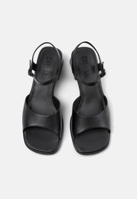 Black leather sandals with slingback strap, square toe, cushioned footbed, and textured insole. Sleek, minimal design. Brand name embossed.