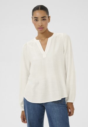 White long-sleeve blouse featuring a V-neck, lightweight fabric, gathered cuffs, and a slightly rounded hem. Paired with blue jeans.