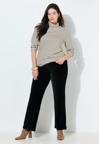 Stribet turtleneck top i beige og sort, parret med sorte fløjlbukser. Modellen har beige ankelstøvler og et tekstureret armbånd på.
