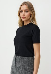 T-shirt nera a maniche corte in morbido tessuto con scollo tondo, abbinata a pantaloni grigi a vita alta con texture. Design semplice e aderente.