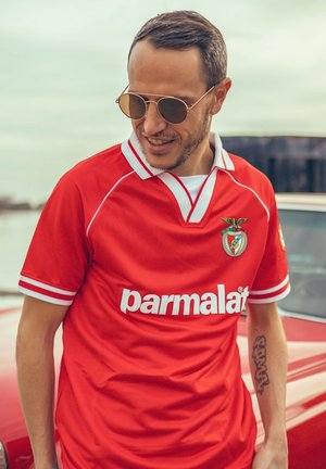 Rode voetbalshirt met witte accenten, met het logo van "parmalat". Korte mouwen, V-hals en een embleemontwerp op de borst. Zonnebril gedragen.