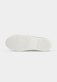 Semelle de chaussure blanche avec une bande de roulement à motif et une section rectangulaire au milieu avec le nom de la marque en relief.