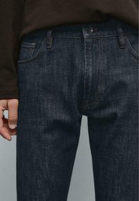 Dunkelblaue Jeans aus Denim mit klassischem geradem Schnitt, fünf Taschen, dezenten Nähten und einem Metallknopfverschluss am Bund.