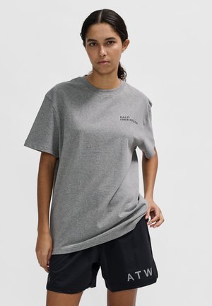 Grijze katoenen t-shirt met korte mouwen en een ronde halslijn, met een zwart gedrukt logo, gecombineerd met zwarte shorts waarop "ATW" in het grijs staat.