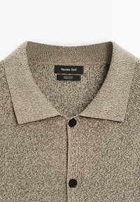 Baumwollhemd von Massimo Dutti, mit einem strukturierten beigen Stoff, klassischem Kragen und drei schwarzen Knöpfen entlang der Vorderleiste.