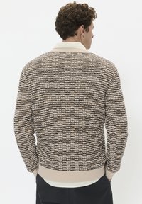 Pulover tricotat în dungi bej și maro, cu un tiv și mansete cu textură ribbată, având un guler crem în contrast. Model texturat pe întreaga suprafață.