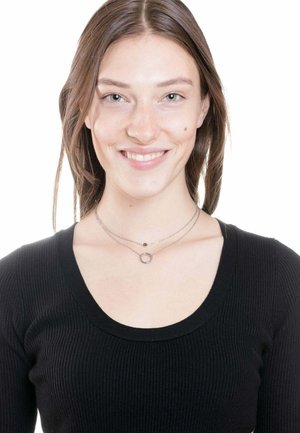 Silberne geschichtete Halsketten mit einem runden Anhänger und einem kleinen runden Pendant, getragen über einem schwarzen gerippten Top mit weiträumigem Ausschnitt.