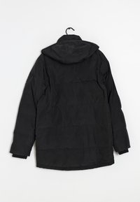 Giacca a vento nera con cappuccio, con polsini a coste, cuciture orizzontali e una texture liscia e opaca. Appesa a un gancio.