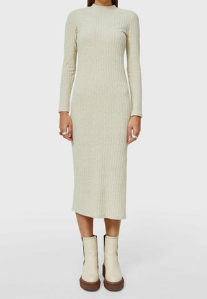 Kvinde iført en beige ribstrikket midi-kjole med lange ærmer og off-white plateau-ankelstøvler med brune såler.