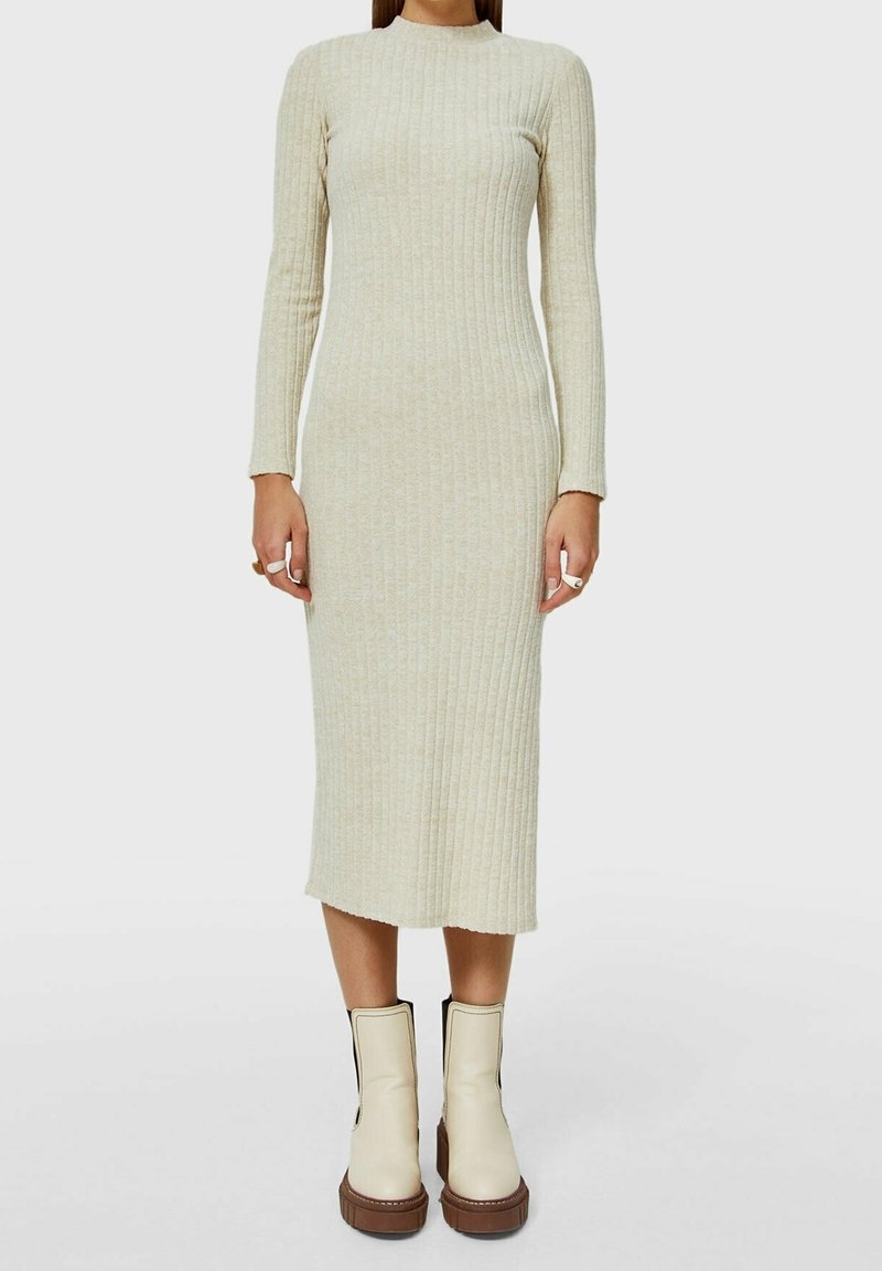 Femme portant une robe midi beige en maille côtelée à manches longues et des bottines à plateforme écrues avec des semelles marron.