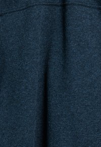 Marineblauwe textiel met een subtiel patroon en lichtblauwe accenten. Het materiaal lijkt zacht met een geweven afwerking, geschikt voor kleding.