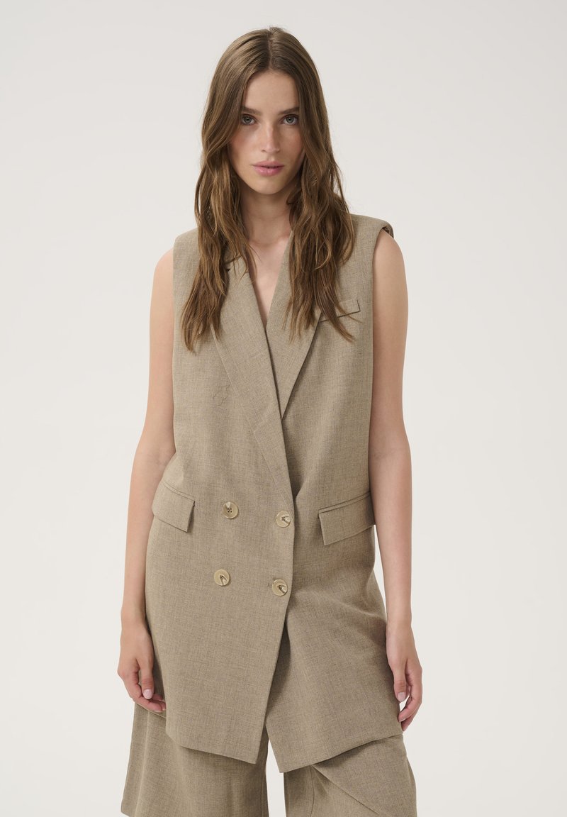 Beige double-breasted vest with two front pockets, made of textured fabric. Features a lapel collar and tailored fit without sleeves.
