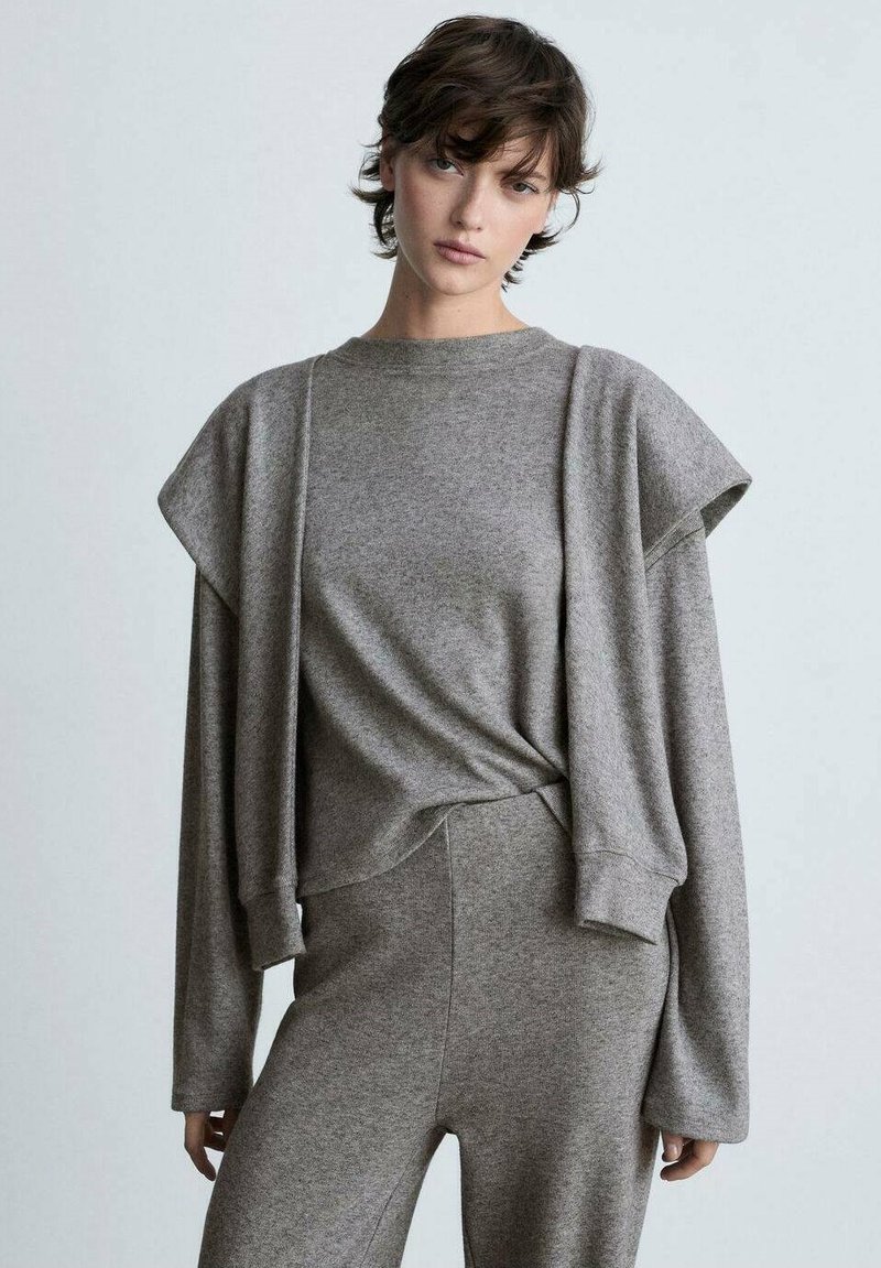 Grauer Strickoberteil mit kurzen, strukturierten Ärmeln, kombiniert mit passenden hochgeschnittenen Hosen. Weicher Stoff und lässiges Design.