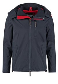 Veste bleu marine avec doublure intérieure rouge, fermeture éclair à l'avant, poche poitrine zippée et capuche attachée avec bandes velcro.