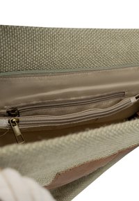 Zielona torba z tkaniny o teksturowym splocie, z beżową podszewką i dwiema kieszeniami na zamek. Brązowy skórzany akcent przy otwarciu.