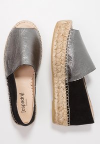 Svarta och metalliska silver espadrillos med en vävd jutesula, öppna sidor och en slät läderöverdel. Påtaglig sömdetalj längs kanten.