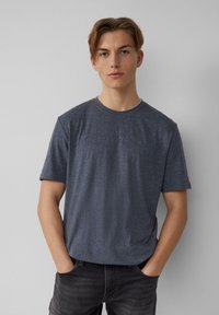 Dunkelgraues Kurzarm-T-Shirt in melierter Textur, mit rundem Ausschnitt, kombiniert mit dunkler grauen Jeans. Einfaches Design, keine sichtbaren Muster oder Akzente.