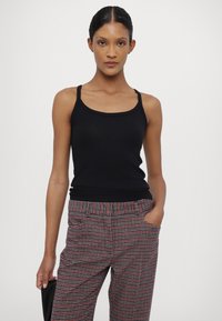 Svart ribbet tank topp med tynne stropper, paret med rød og grå rutete bukser med elastisk midje og sidelommer.