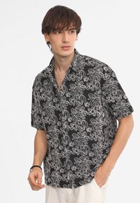 Maglietta nera a maniche corte con motivi floreali bianchi. Collo button-down, vestibilità rilassata, texture morbida e dettagli sottili sulle maniche.
