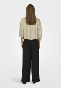 Afkortet beige top med løse ærmer, parret med høj talje sorte brede bukser. Glat tekstur og neutral farvepalette.