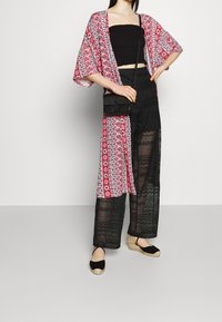 Kimono long, rouge et blanc à motifs posé sur un crop top noir, associé à un pantalon en dentelle noir et des espadrilles noires. Sac bandoulière noir.