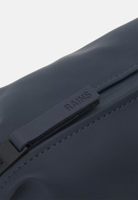 Marine vanntett bag med glatt tekstur, med svart glidelås og preget "RAINS"-logo på glideren. Minimalistisk design.