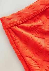 Serviette orange avec des motifs de coquillage texturés, dotée d'une taille lisse et d'une finition en tissu doux et pelucheux.