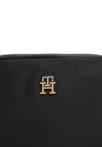 Black nylon bag featuring a gold 'TH' logo accent. Smooth texture with a structured shape and minimalistic design.