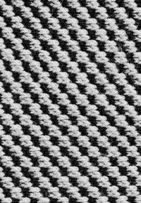 Tessuto intrecciato con un motivo a chevron in bianco e nero, con una superficie testurizzata e fibre visibili.