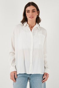 White long-sleeve shirt with textured fabric, button-down front, and single chest pocket. Paired with light blue denim jeans.