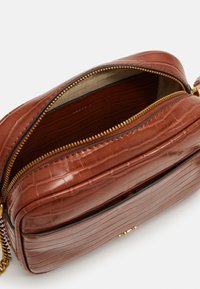 Brązowa torebka crossbody z tłoczonej skóry w krokodyla z złotym zamkiem, podwójnymi przegródkami i gładką podszewką.