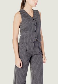 Gilet grigio a righe sottili con scollo a V, caratterizzato da cinque bottoni neri e tasche laterali, abbinato a pantaloni a gamba larga coordinati.