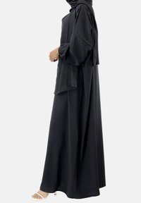 Zwarte maxi jurk met lange mouwen, een gedrapeerde voorkant en een capuchon. Gemaakt van lichte stof met een vloeiende silhouette en minimale accenten.