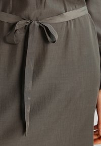 Robe grise à la texture lisse, taille cintrée avec une ceinture en tissu nouée sur le côté, et un design simple et élégant.