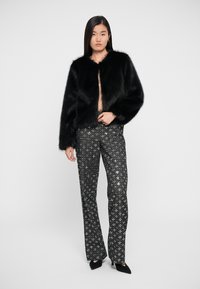 Zwarte nepbontjacket met een ronde hals en cropped mouwen, gecombineerd met high-waisted zwarte broeken met zilveren sterpatronen.