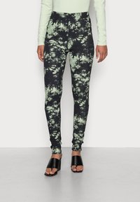Svart och grön tie-dye leggings med hög midja, utrustad med en texturerad tyg och smal passform. Kombineras med svarta öppen-tå skor.