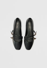 Scarpe Mary Jane nere in pelle con punta quadrata, dotate di doppie cinghie alla caviglia e fibbie in tono oro. Texture liscia e design minimalista.