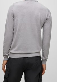 Szary pulower z długim rękawem o gładkiej fakturze, z prążkowanymi mankietami i dolnym brzegiem, z klasycznym kołnierzykiem. Noszony z czarnymi spodniami typu cargo.