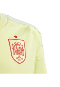 Yellow athletic jersey featuring a red embroidered crest with a crown and the year “1909” below. White stripes on the collar and sleeves.
