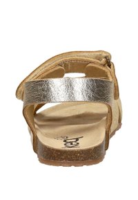 Open-achter sandaal met metalen bandje en kurken zool, zichtbare beige voetbed met getextureerde bruine buitenzool, gezien vanaf de hielzijde.