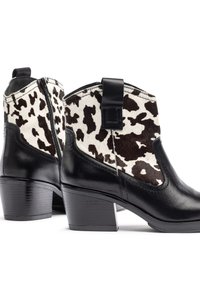 Botines de cuero negro con paneles de piel de vaca que presentan un patrón moteado en blanco y negro. Tacones gruesos y cremalleras laterales para facilitar su uso.