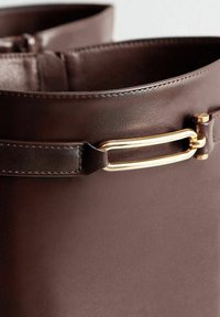 Close-up of dark brown leather boot with gold rectangular buckle detail near the top edge.