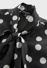 Blouse noire à gros pois blancs, avec un col à nœud et une étiquette portant la mention « Tabitha Simmons Next » à l’intérieur de l’encolure.