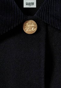 Manteau en laine noir avec un col côtelé et un bouton circulaire doré portant le texte en relief "Claudié Pierlot" à l'avant.
