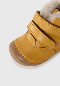 Gul lær toddler sko med doble borrelåsremmer, myk beige pelskledd innside og lysebrun gummisåle på hvit bakgrunn.